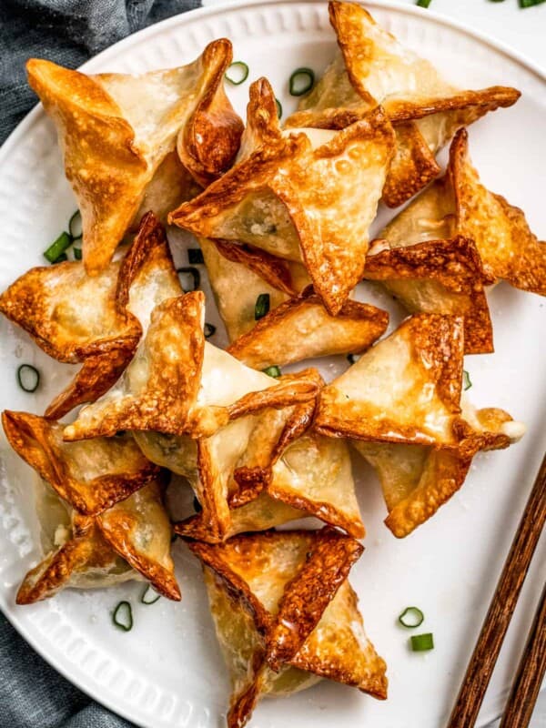 Air Fryer Crab rangoon on a white plate garnished with green onions and a pair of chopsticks placed next to the rangoons.