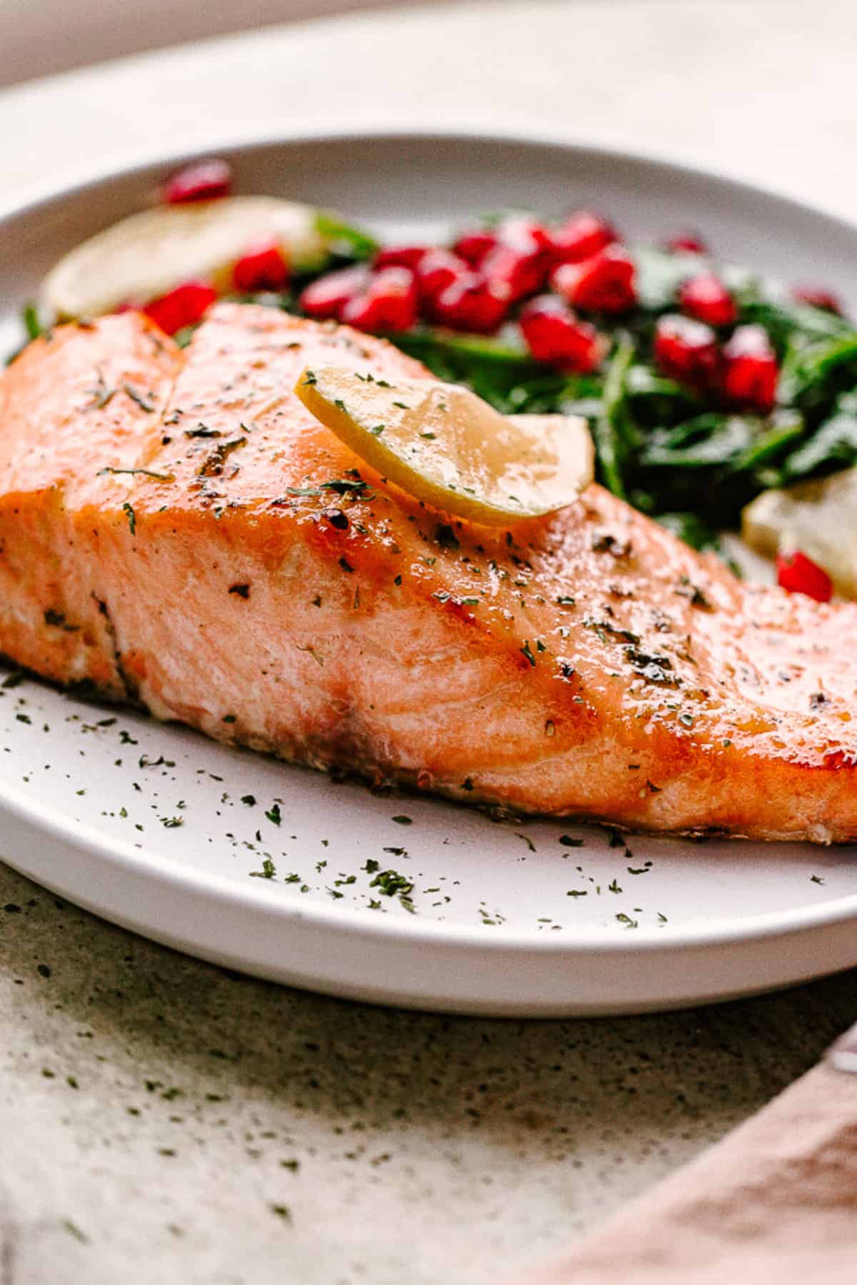 Flakey cooked salmon on a plate with lemon and veggies.