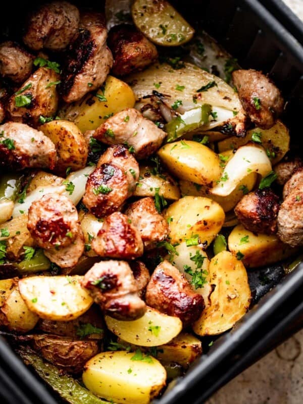 rounds of sausage, cut up baby potatoes, peppers, and sliced onions arranged in an air fryer basket