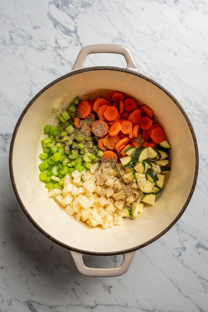 Adding celery, carrots, zucchini, and potato to sauteed onions and garlic in a soup pot.