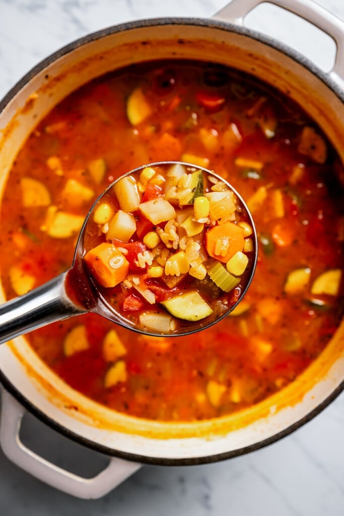 A ladle holding a scoop of alphabet soup up to the camera.