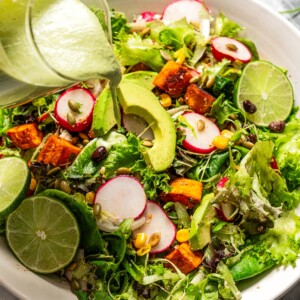 Pouring avocado lime ranch dressing over a salad.