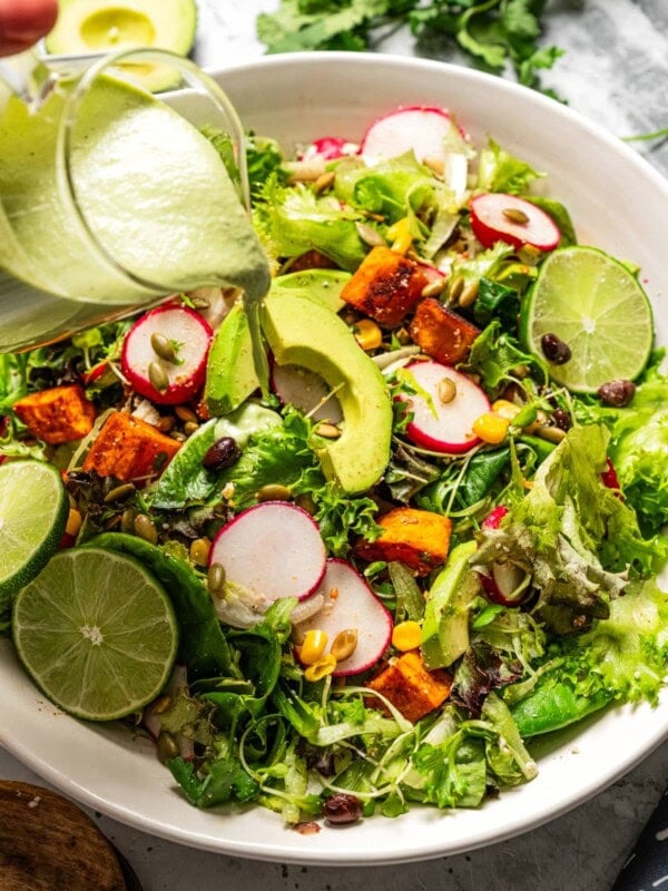 Pouring avocado lime ranch dressing over a salad.