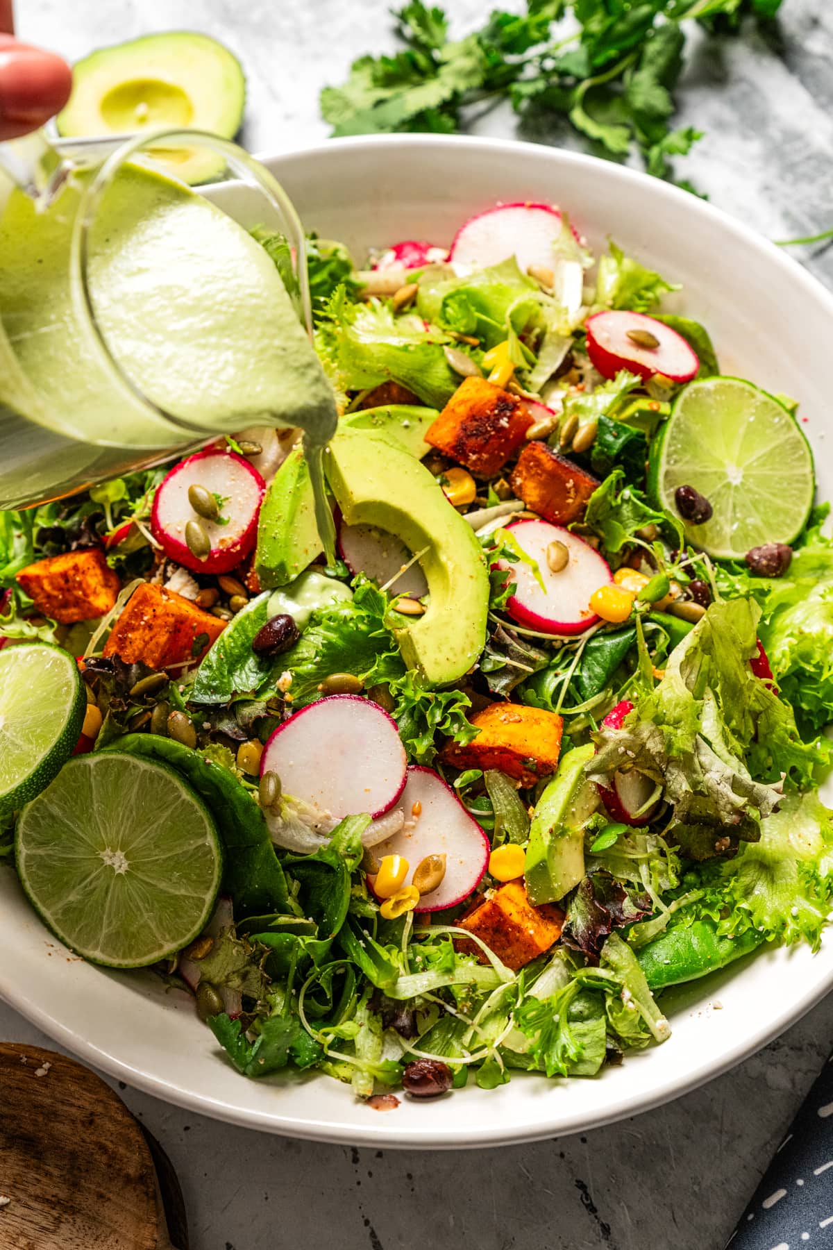 Pouring avocado lime ranch dressing over a salad.