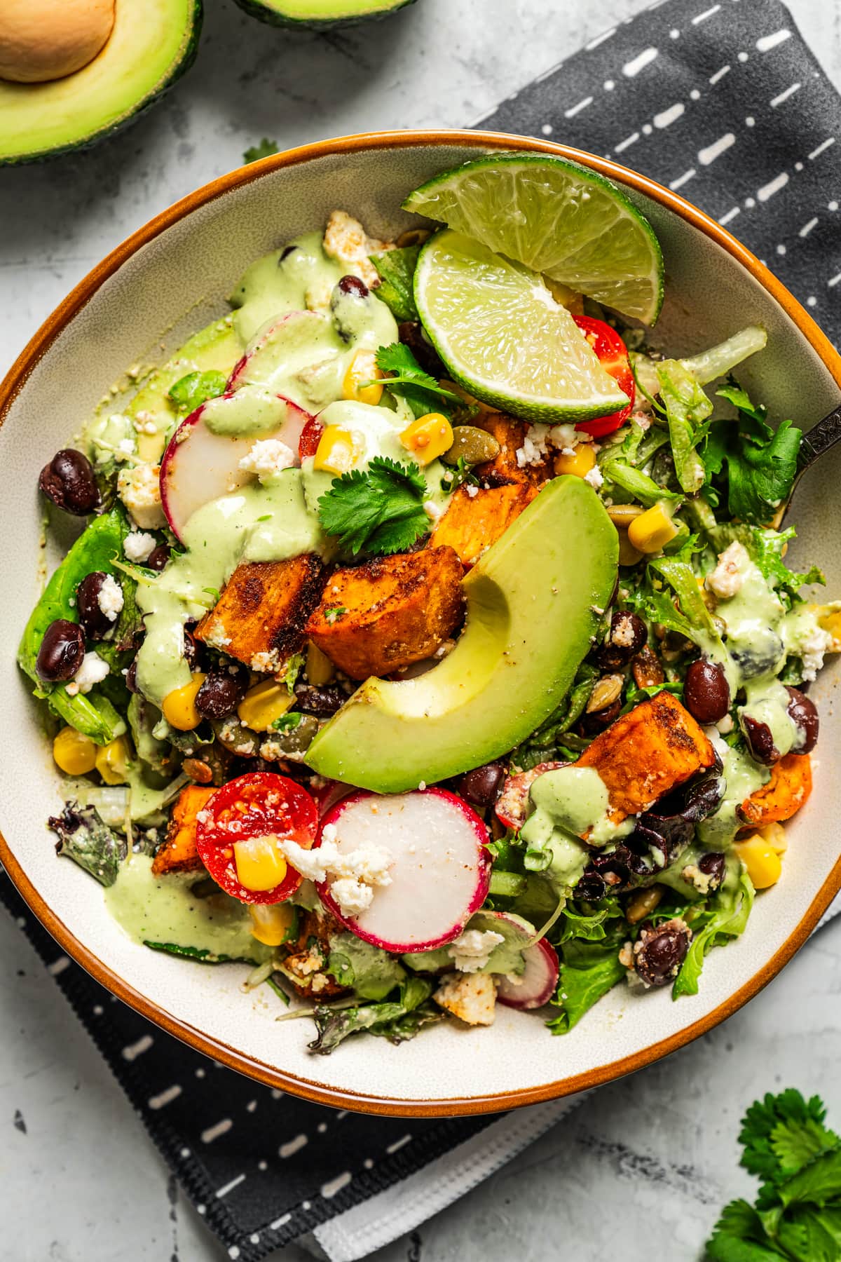 Overhead image of salad with avocado lime ranch dressing served in a bowl near an avocado.