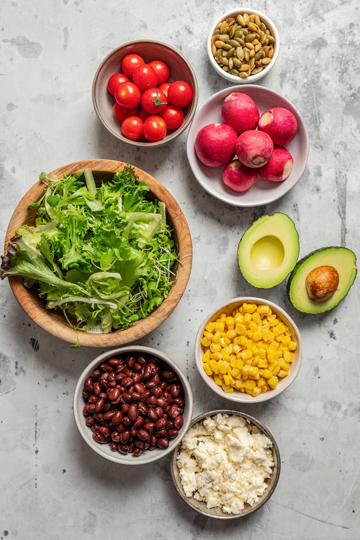 Veggies, greens, black beans, queso fresco, pepitas, and avocado in separate bowls.