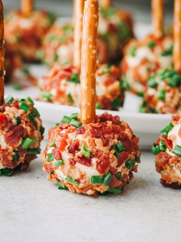 A close-up of mini cheeseballs sprinkled with bacon and chives and a pretzel stick going through the center of each cheeseball.