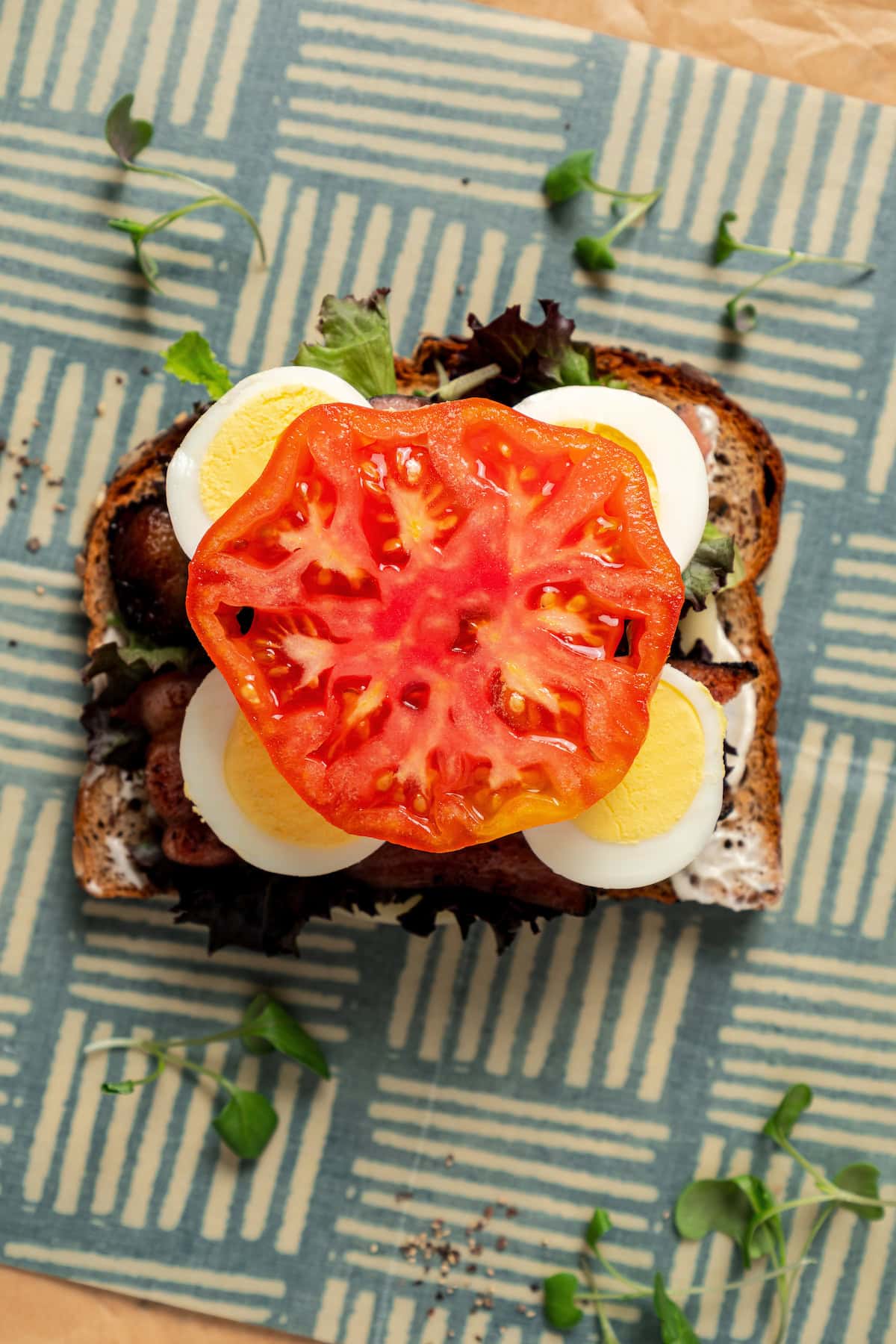 Layering sliced hard boiled egg and a slice of tomato into a sandwich.