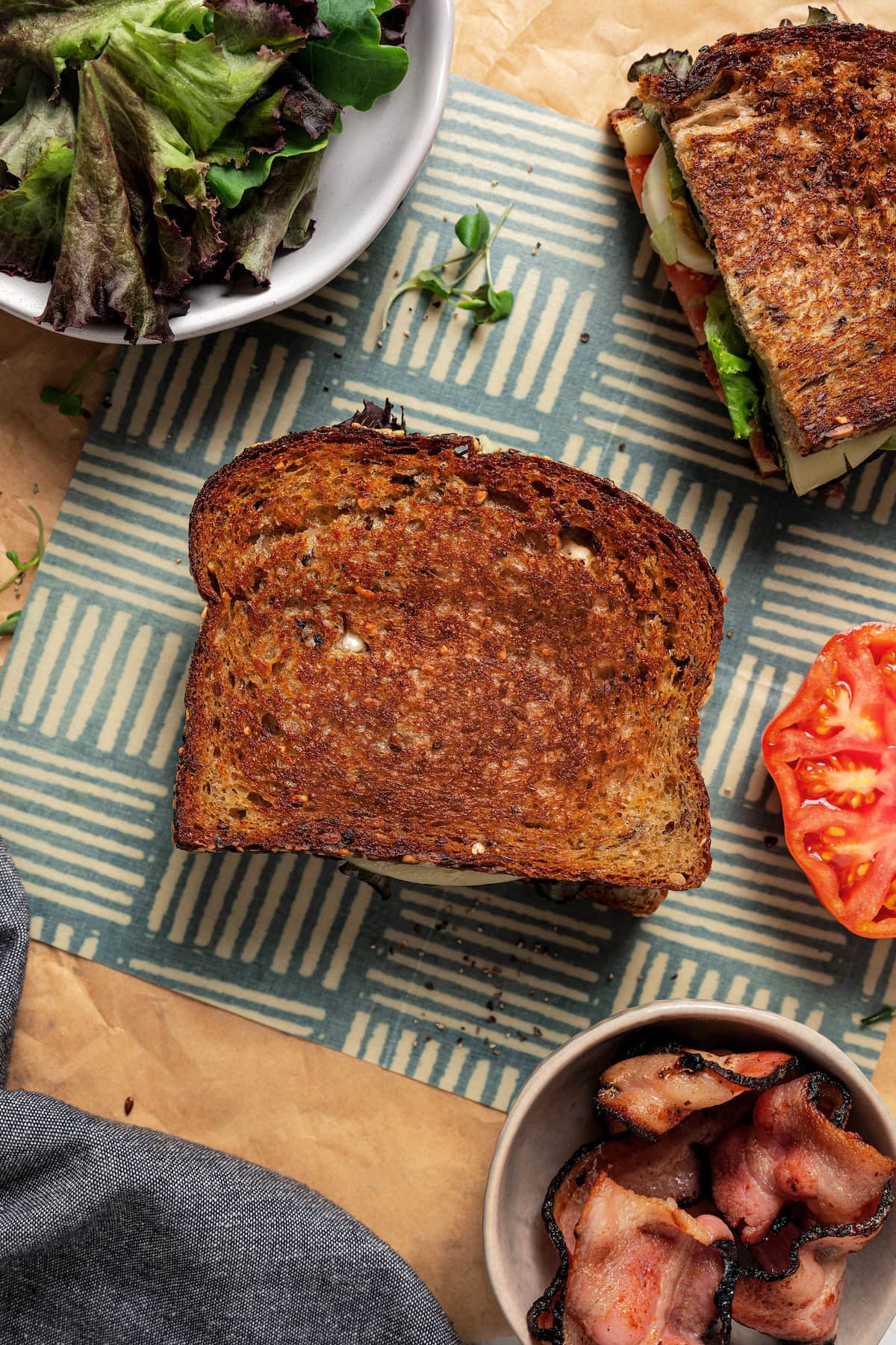 Overhead image of a bacon, egg, and cheese grilled cheese near a bowl of lettuce.