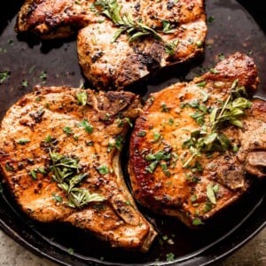 overhead shot of three oven baked pork chops arranged on a cast iron skillet and garnished with fresh herbs