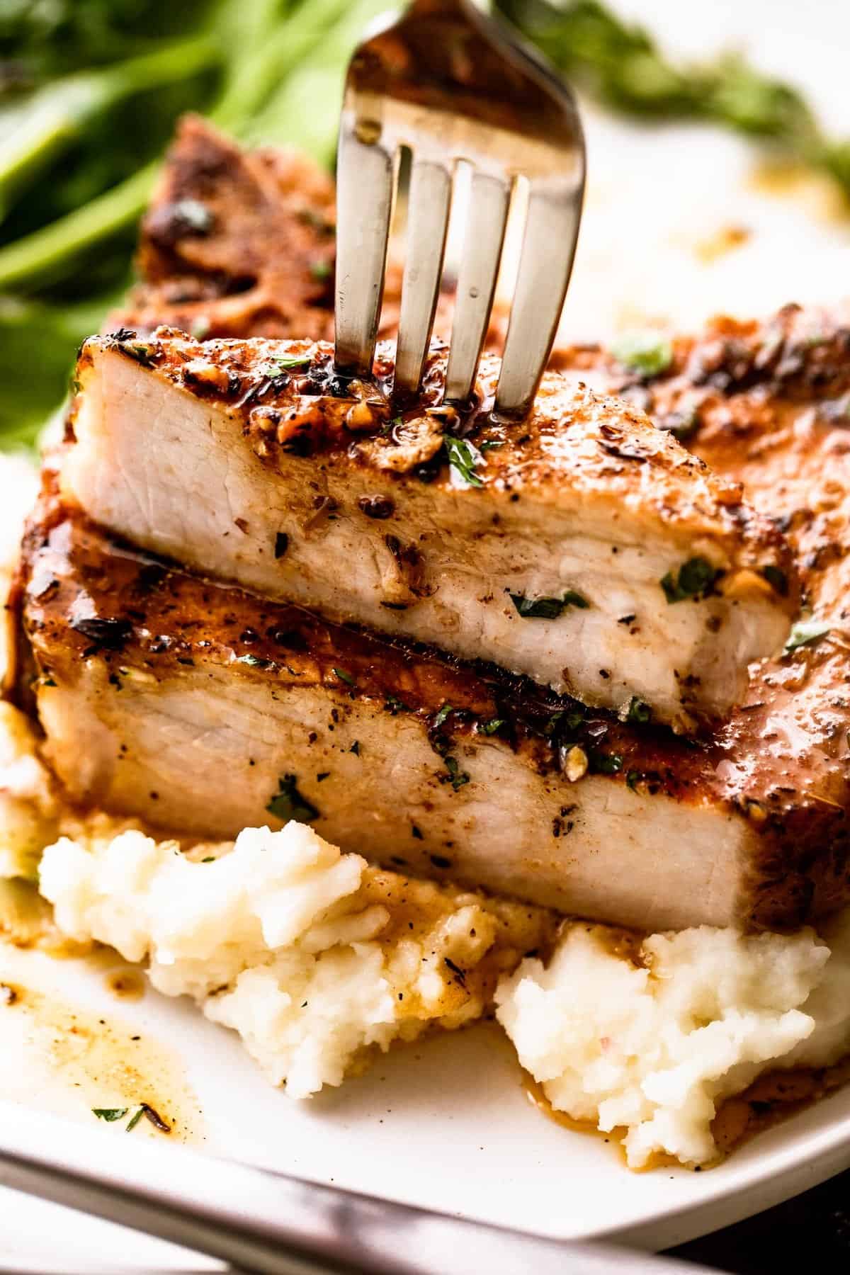 fork stabbing through a halved pork chop set on a bed of mashed potatoes