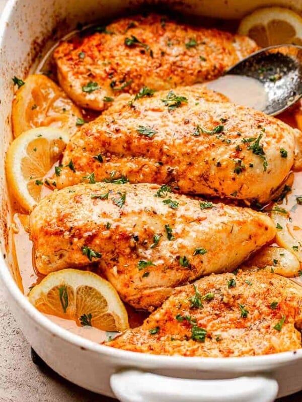 baked chicken breasts set over lemon slices in a baking dish