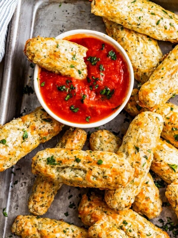 Overhead shot of homemade baked mozzarella sticks on a tray with a bowl of marinara sauce.