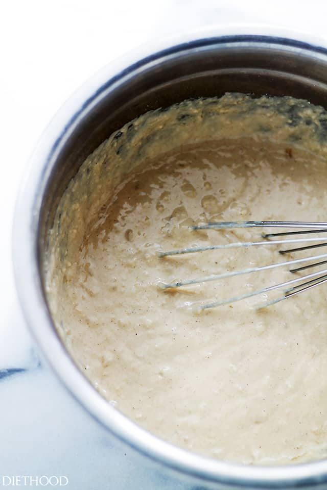 A whisk resting in banana bread waffle batter in a metal bowl.