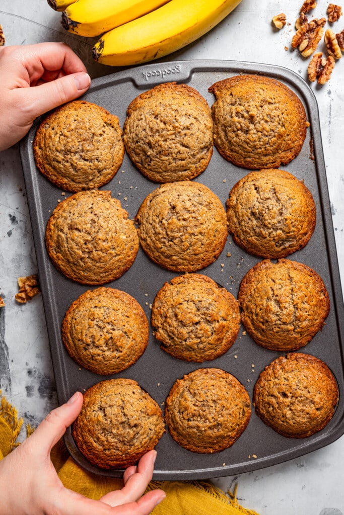 Two hands holding a muffin pan full of muffins.