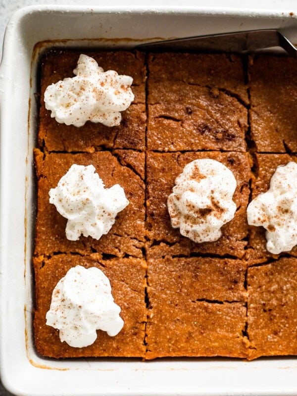 A square baking dish with pumpkin bars in it, topped with a swirl of whipped cream.