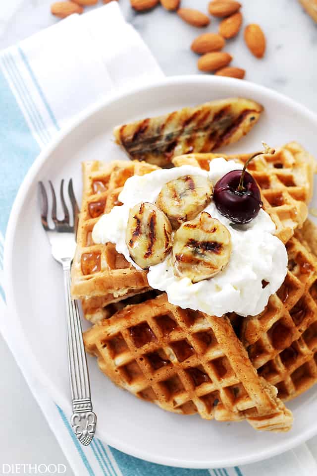 Overhead view of a stack of banana bread waffles topped with whipped cream and grilled banana slices on a white plate.