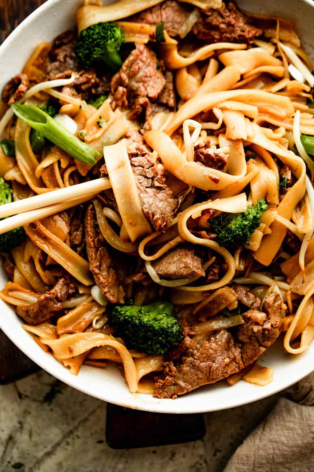 overhead shot of chopsticks rotating wide rice noodles and flank steak.