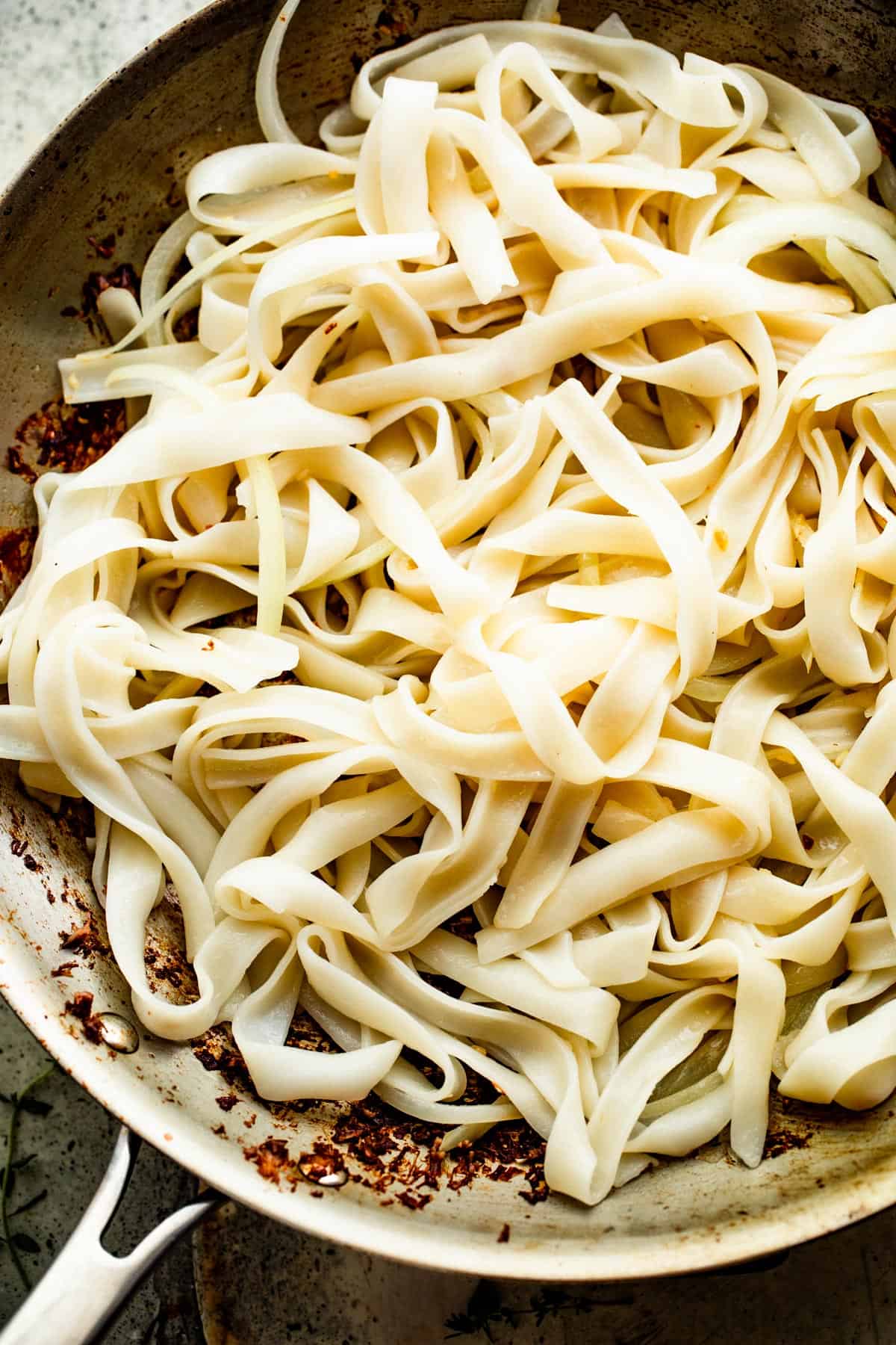 tossing wide rice noodles in a skillet.