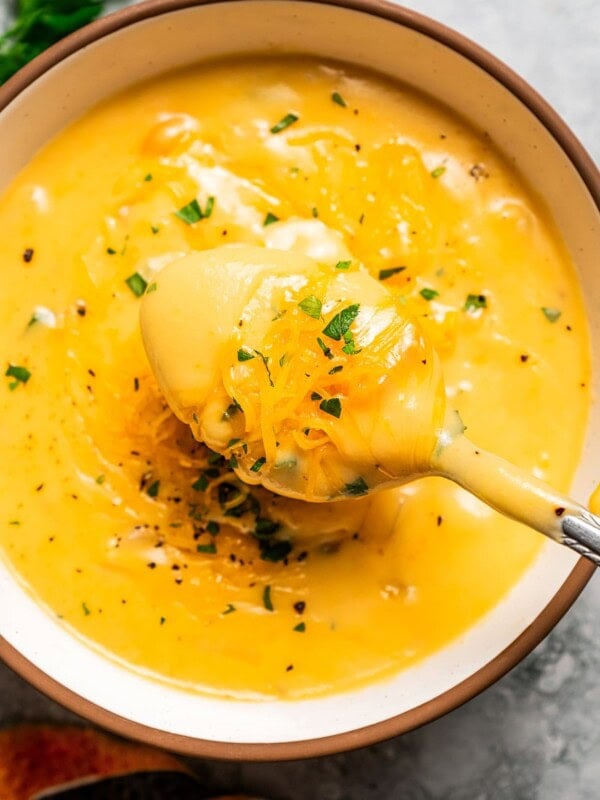 Close up overhead view of a spoonful held over a bowl of beer cheese soup garnished with chopped parsley on a countertop.