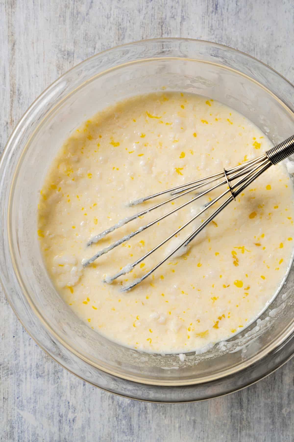 Wet ingredients combined in a glass bowl with a whisk.