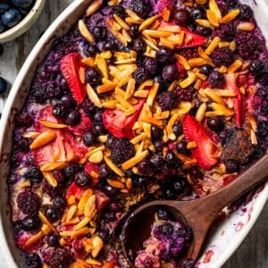 Overhead view of baked berry oatmeal in an oval casserole dish with a wooden spoon.