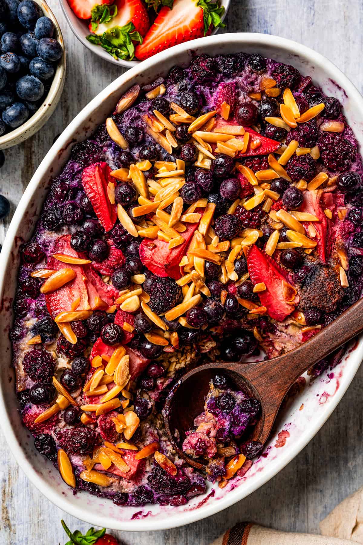 Overhead view of baked berry oatmeal in an oval casserole dish with a wooden spoon.