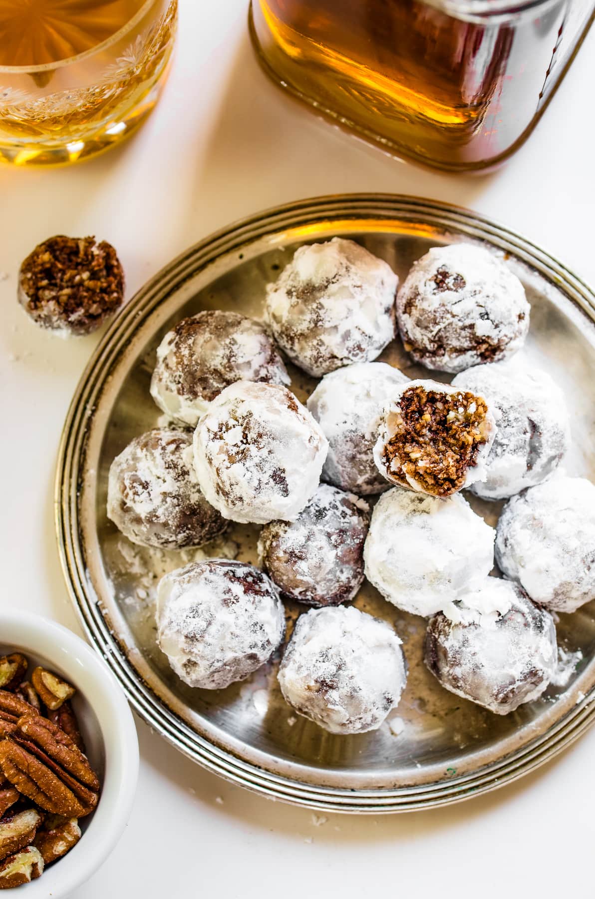 Aerial view of Bourbon Balls served on a platter, with a bottle of alcohol and a bowl of pecans arranged around the platter.