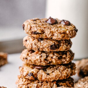 A stack of banana chocolate chip cookies with a milk carafe in the background.