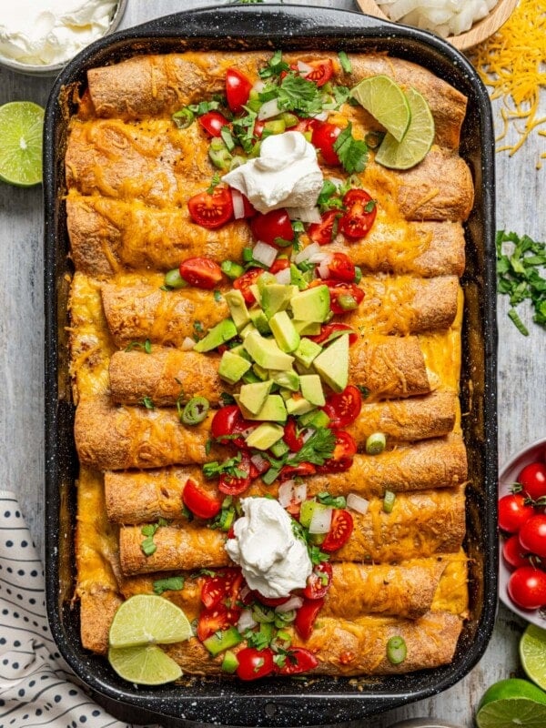 Enchiladas in the baking dish with cilantro, sour cream, tomatoes, chilis, and avocado.