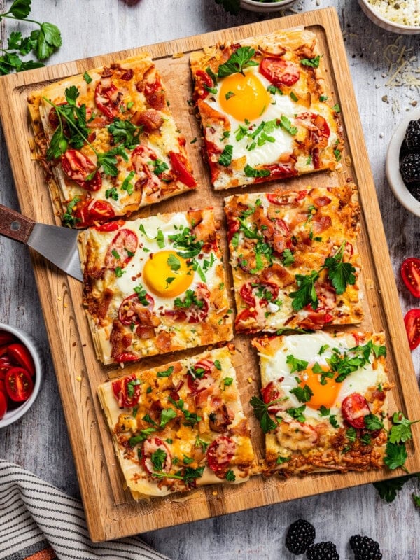 Sliced phyllo pizza with soft eggs, bacon, and tomatoes on a cutting board.