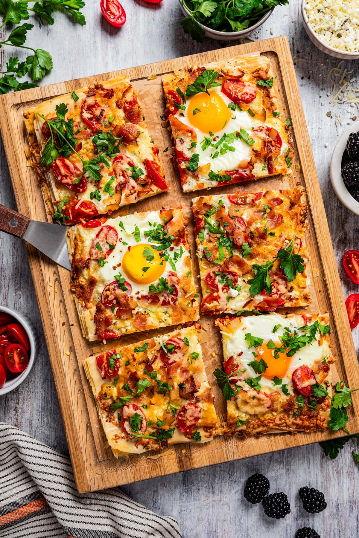 Sliced phyllo pizza with soft eggs, bacon, and tomatoes on a cutting board.