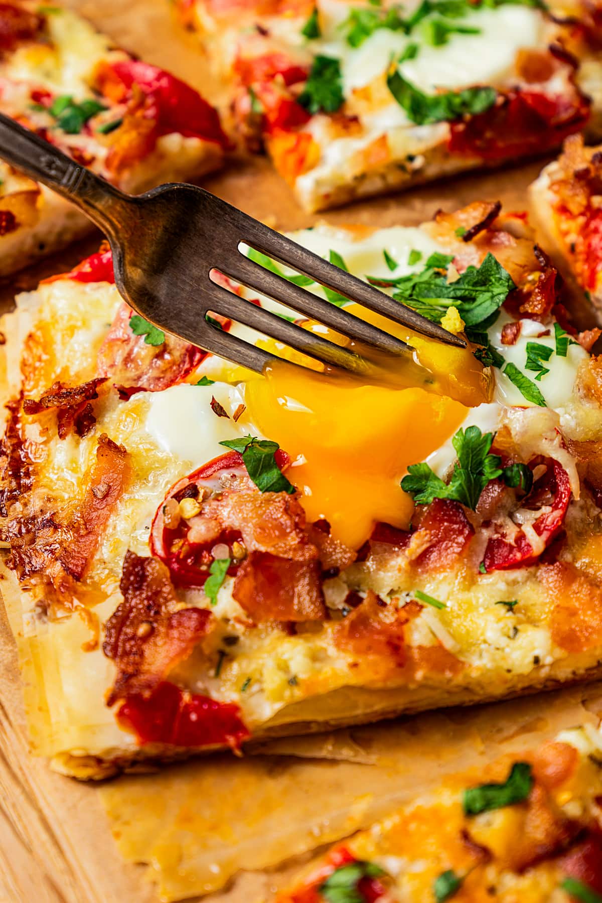 A fork bursting the yolk of an egg on a slice of pizza.