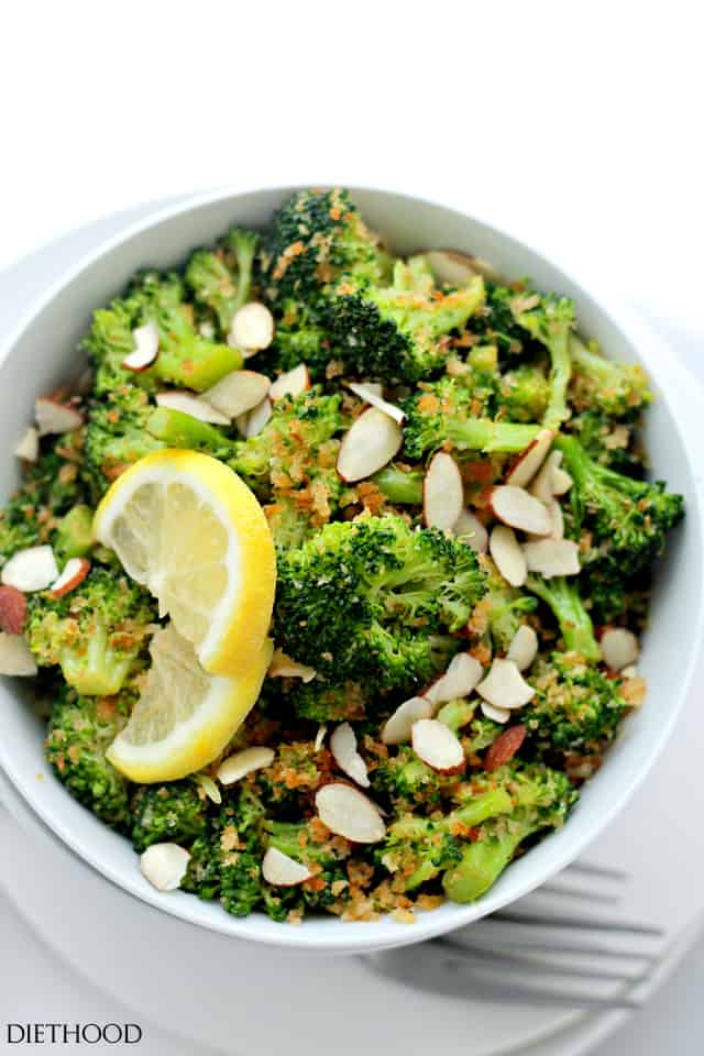 Overhead photo of a bowl of cooked broccoli with garlic panko mixture, a lemon wedge, and sliced almonds. 