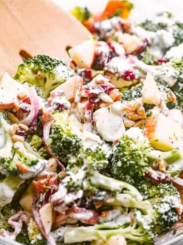 side shot of tossing broccoli apple salad with wooden salad forks