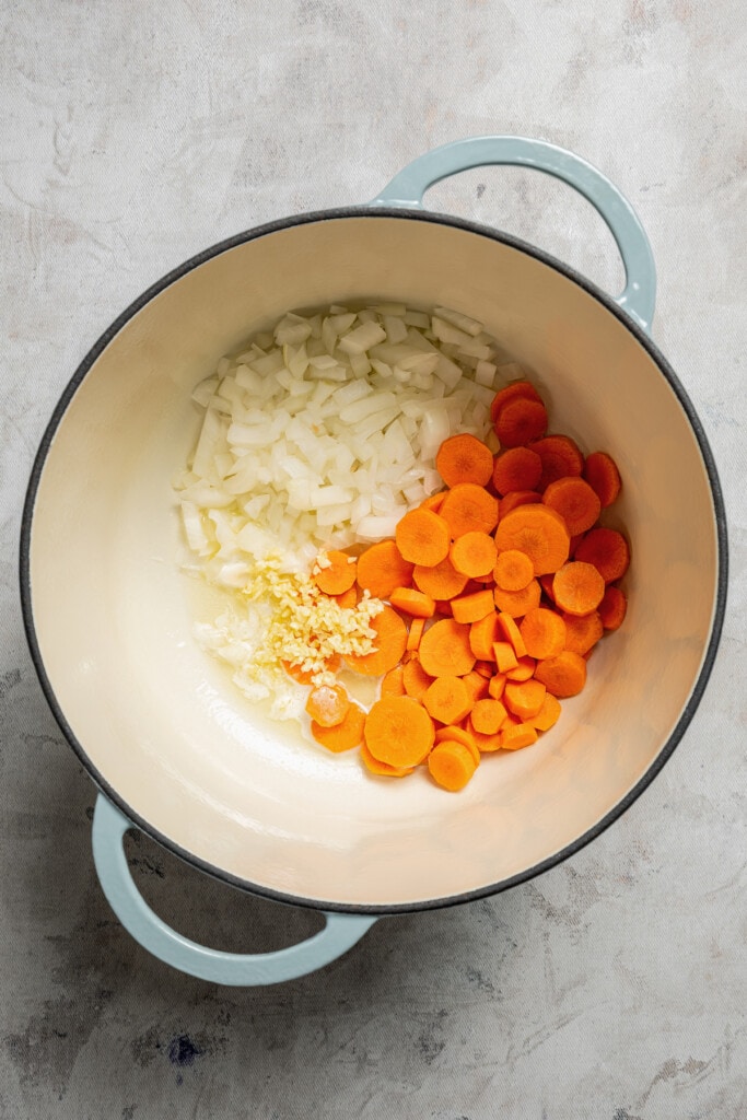 Adding onions, carrots, and garlic to a soup pot.