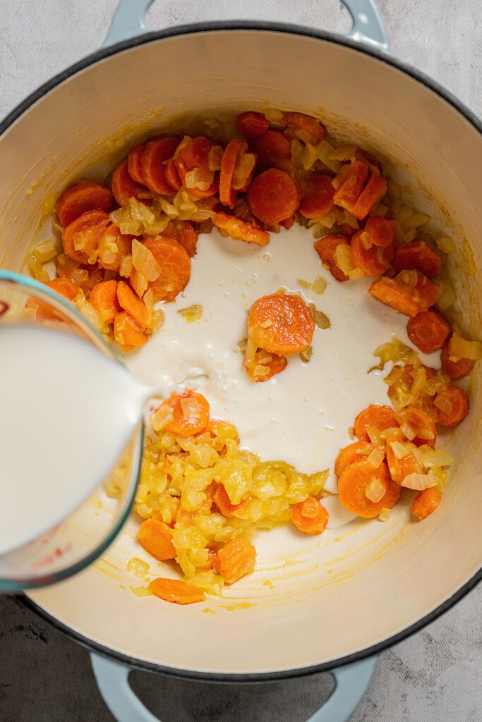 Pouring milk into a soup pot with sauteed veggies and roux.