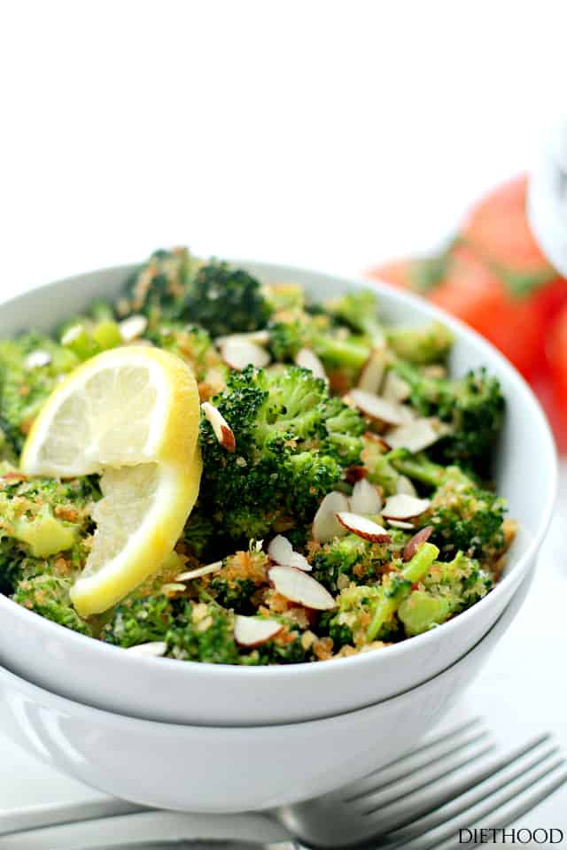 Bowl of garlic steamed broccoli with sliced almonds and a lemon wedge.