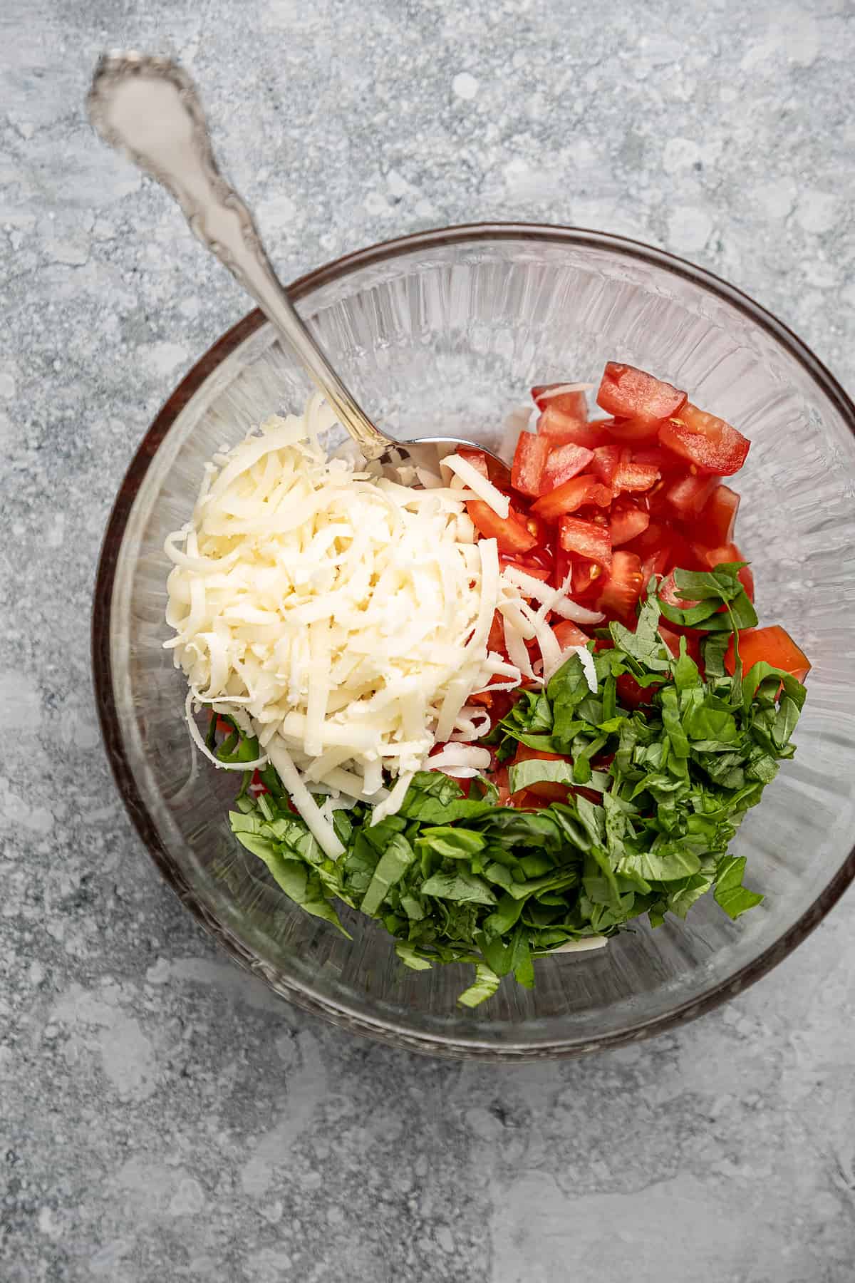 Shredded mozzarella, diced tomatoes, and basil ribbons combined in a mixing bowl with a fork.