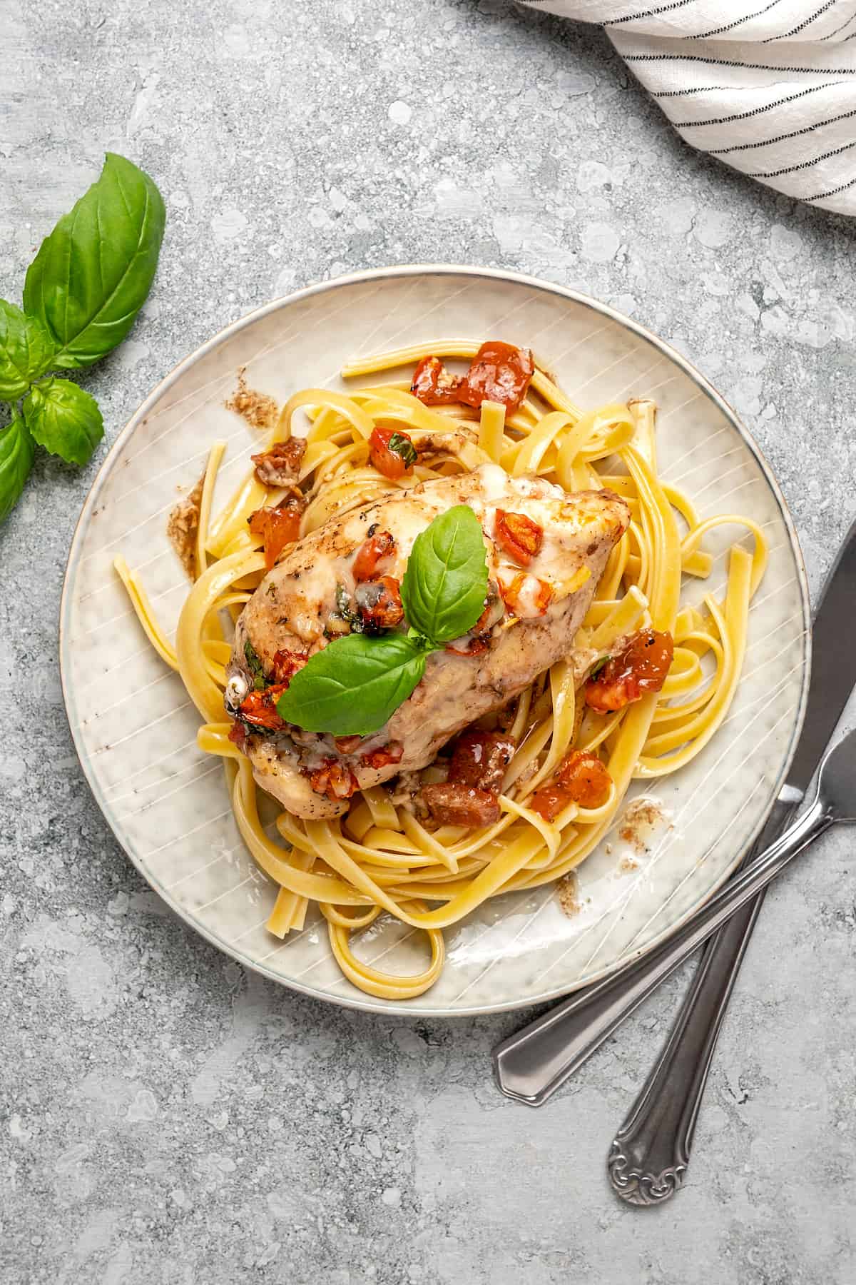 Top view of stuffed chicken breast served over a plate of pasta, garnished with basil leaves.