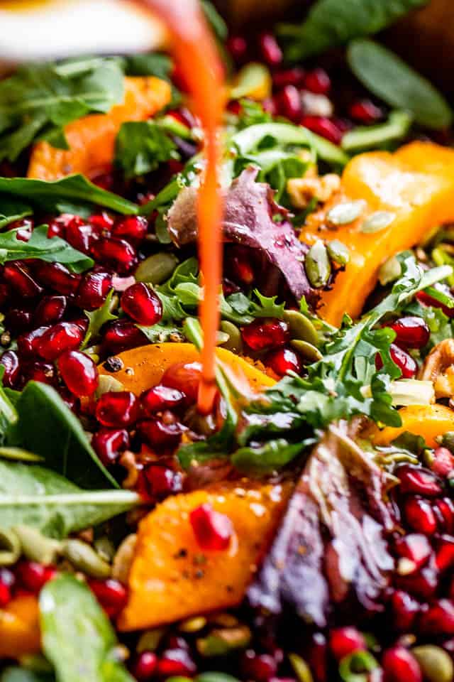 pouring pomegranate salad dressing over butternut squash salad