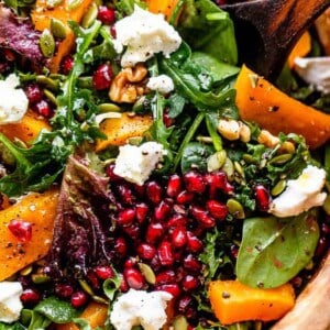 close up shot of salad greens topped with squash, pomegranate arils, nuts, and goat cheese