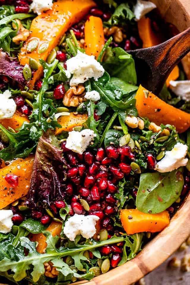 close up shot of salad greens topped with squash, pomegranate arils, nuts, and goat cheese