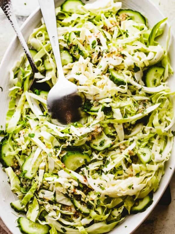 Cabbage Cucumber Salad served on an oblong serving plate with a large fork and spoon placed in the center of the salad.