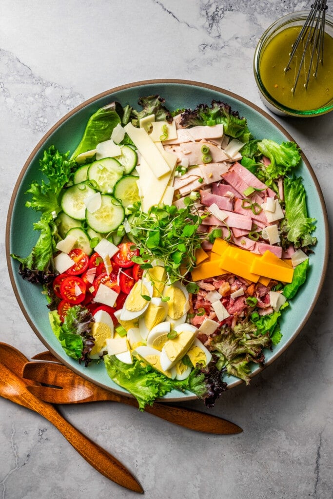 Chef salad ingredients arranged over the top of a large bowl of greens.