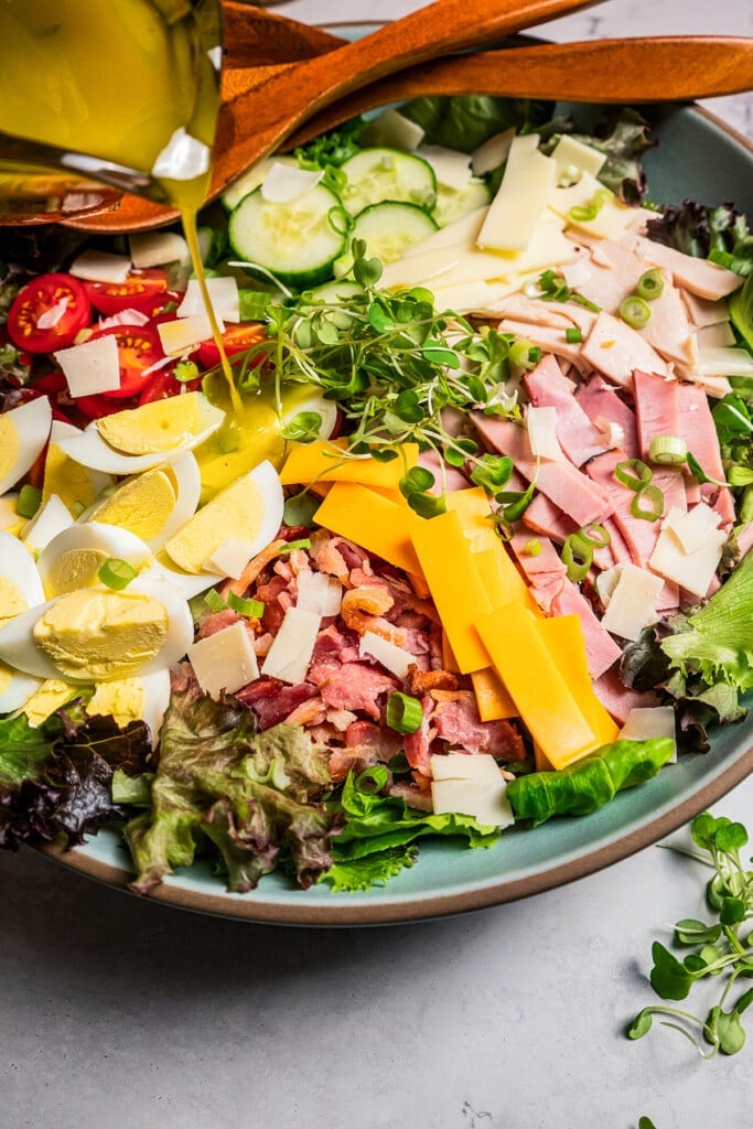 Italian dressing is poured over a chef salad in a large salad bowl.