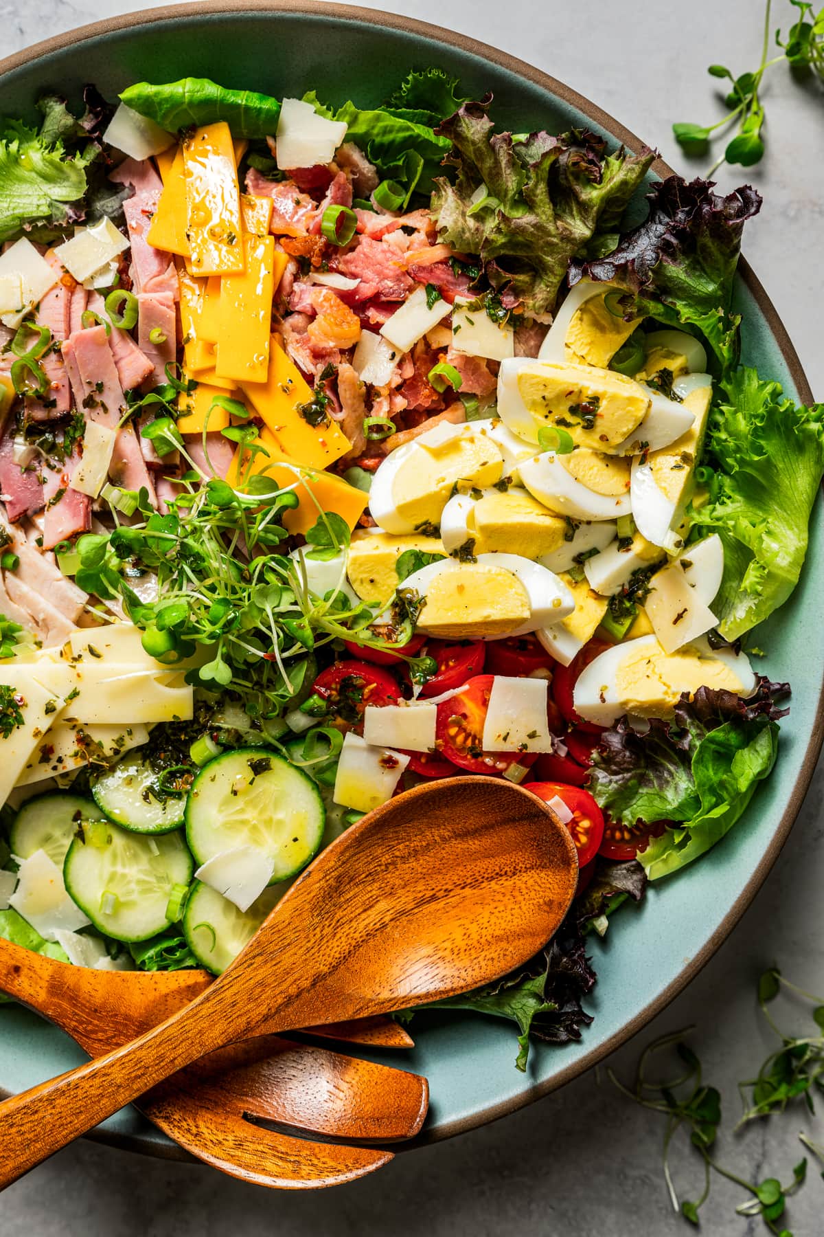 Chef salad in a large salad bowl dressed in Italian dressing, next to wooden salad tongs.