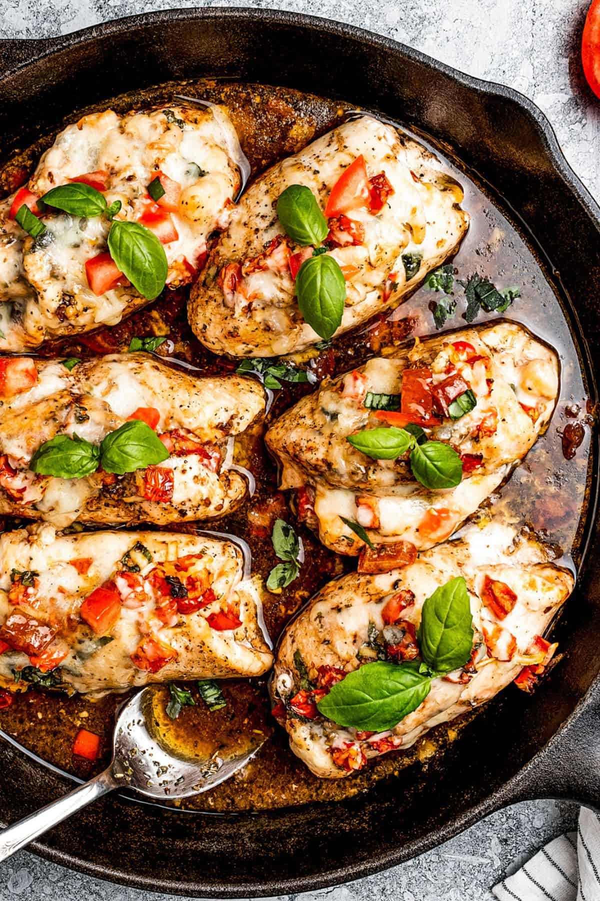 Six stuffed chicken rollups, garnished with diced tomatoes and fresh basil leaves, and arranged in a skillet.