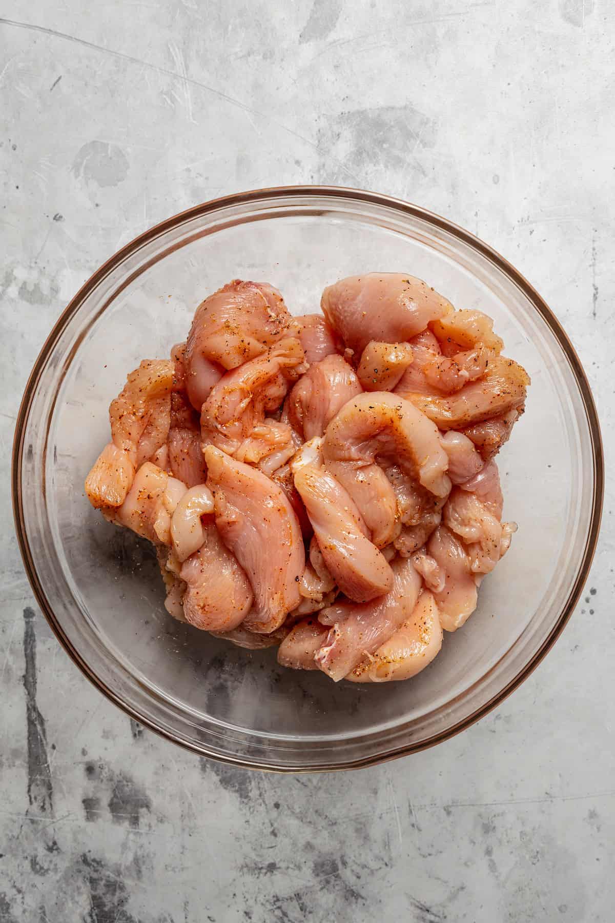 Seasoned uncooked chicken strips in a glass bowl.