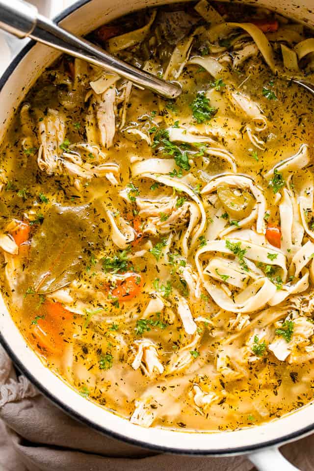 Close-up overhead shot of chicken noodle soup in a white Dutch oven.